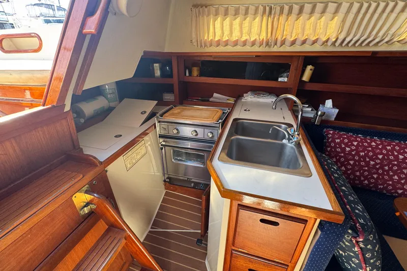 Interior of 1985 Catalina 38 sailboat kitchen with stove, sink, and wooden cabinetry.