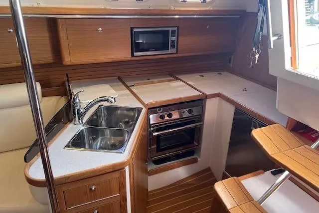 2016 Catalina 385 yacht kitchen with wood cabinetry, stainless steel sink, oven, and microwave.