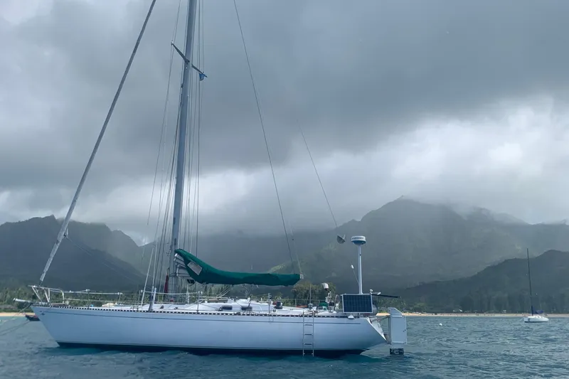 Sailboat Tartan 41 (1972) anchored with mountainous backdrop under cloudy skies.