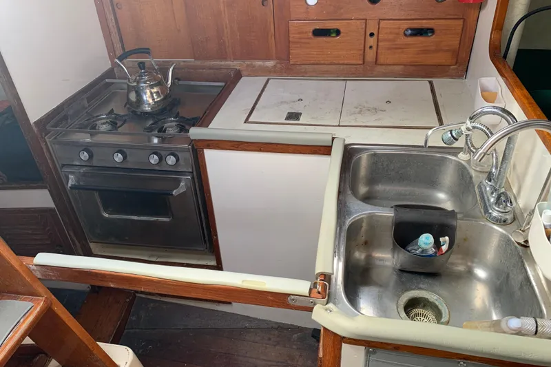 1972 Tartan 41 yacht kitchen with stove, sink, and wooden cabinetry.
