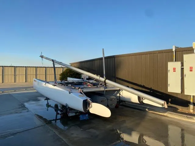 1989 Nacra 5.8 catamaran on trailer, parked near industrial building under clear sky.