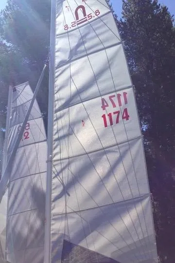 Sailboat with Nacra 5.8 sails, model year 1989, against a forest backdrop.
