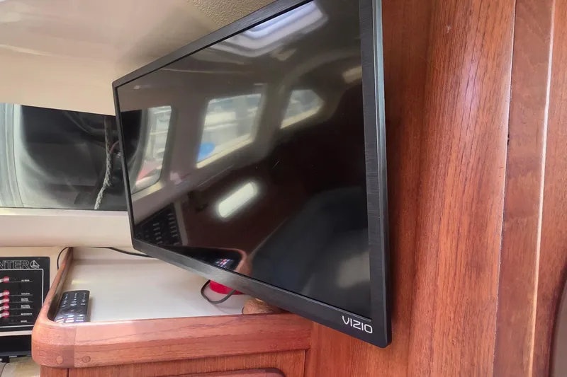 Flat-screen TV inside a 1995 Hunter 336 sailboat cabin, mounted on wooden paneling.