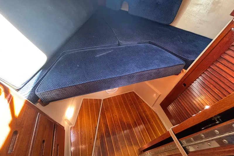 1988 Catalina 34 sailboat interior with blue cushioned V-berth and wooden flooring.