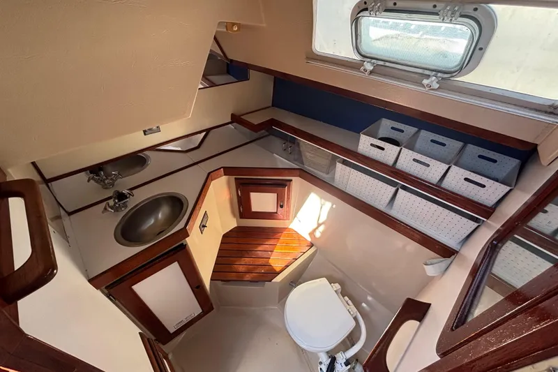 1988 Catalina 34 yacht bathroom with sink, toilet, storage bins, and wooden accents.