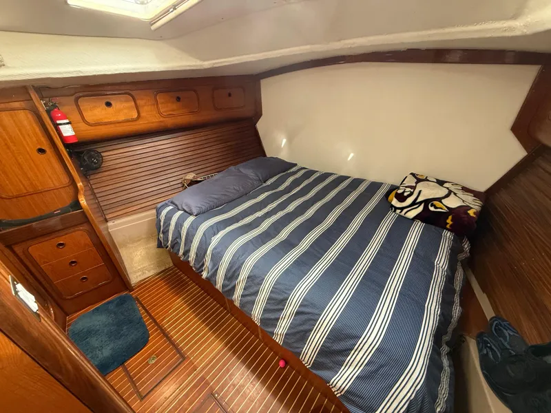 Cozy cabin interior of 1986 Beneteau Idylle 15.50 sailboat with striped bedding and wooden finish.