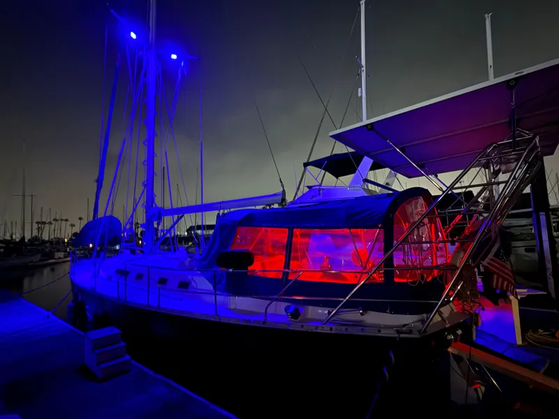 Beneteau Idylle 15.50 sailboat illuminated with blue and red lights at night, docked in a marina.