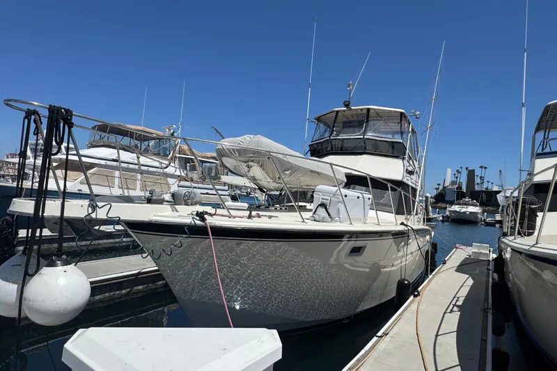 1985 Hatteras 45 Convertible yacht docked at marina under clear blue sky.