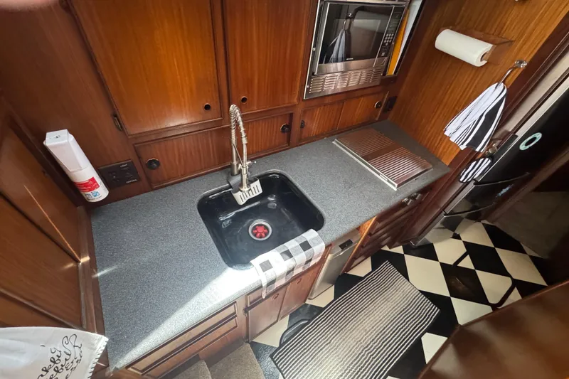 Galley kitchen in 1985 Hatteras 45 Convertible yacht with wood cabinetry and checkered floor.