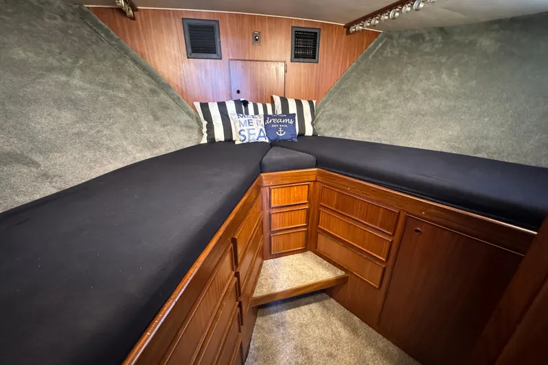 Interior cabin of 1985 Hatteras 45 Convertible yacht with cozy bedding and wooden cabinetry.