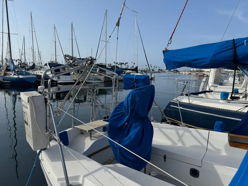 1990 Catalina 30 MkII sailboat docked in marina, blue covers, calm water, clear sky.