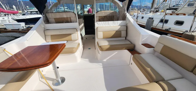 2012 Tiara Yachts 3100 Coronet interior with beige seating and wooden table, docked at marina.