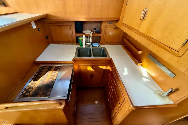 Compact wooden kitchen interior of 1990 Mikelson 42 boat with sink and stove.