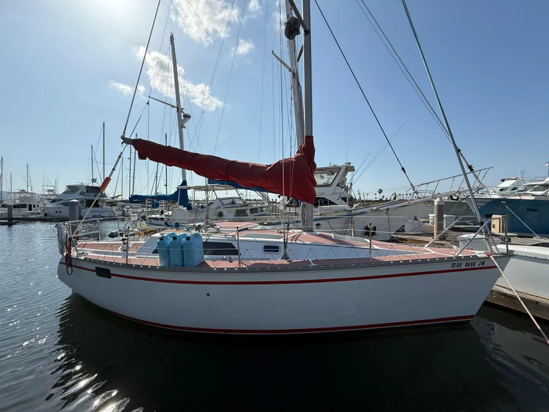 1989 Hunter 30 sailboat docked in marina, featuring red sail cover and clear blue sky.