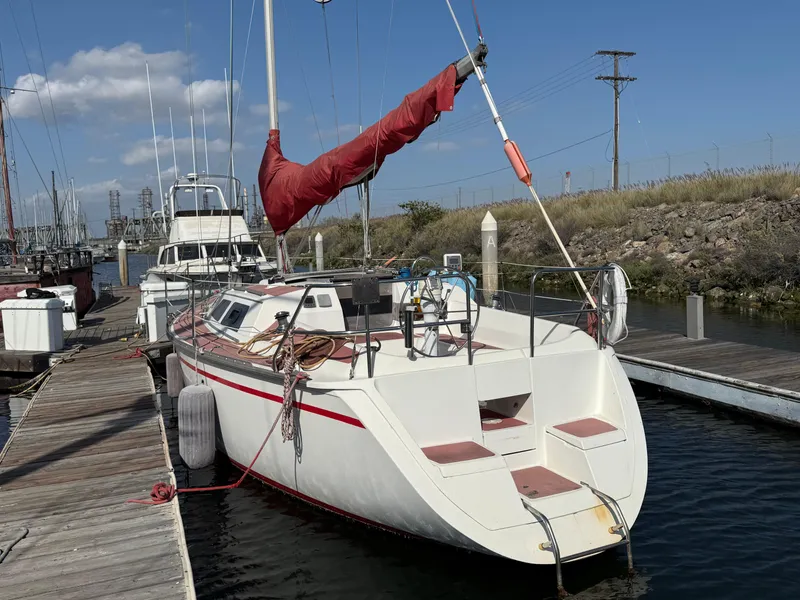 1989 Hunter 30 sailboat docked, featuring red sail and white hull, under clear blue sky.