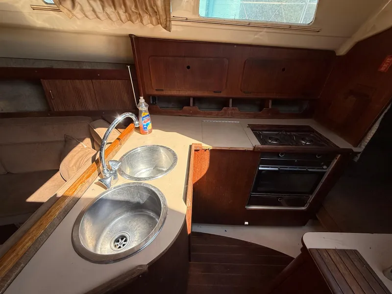 Interior of 1989 Hunter 30 sailboat kitchen with sink, stove, and wooden cabinetry.