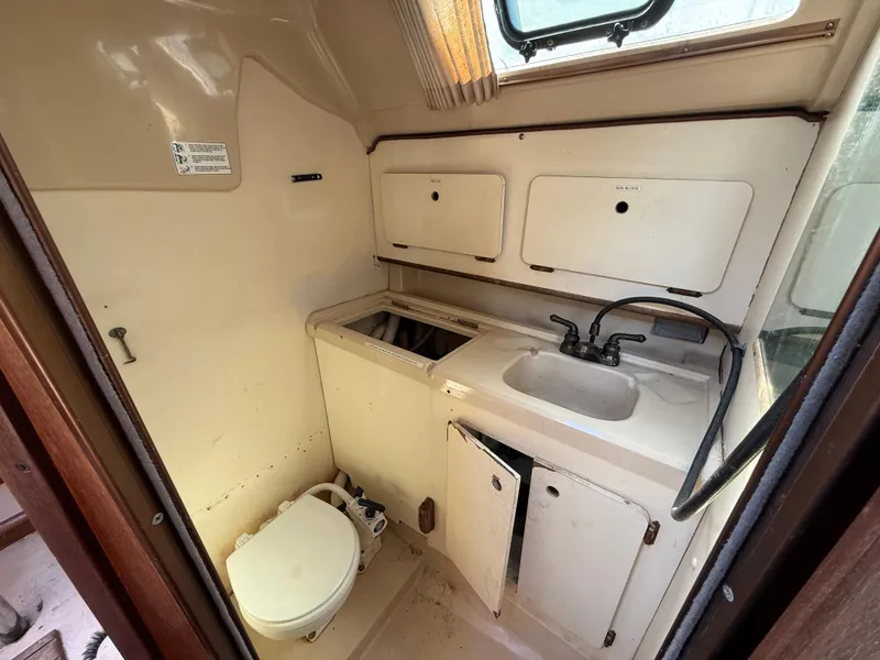 Compact bathroom in a 1989 Hunter 30 sailboat with sink, toilet, and storage cabinets.