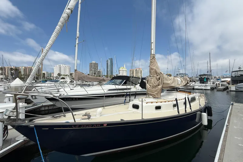 1957 Rhodes Bounty sailboat docked in marina with city skyline background.