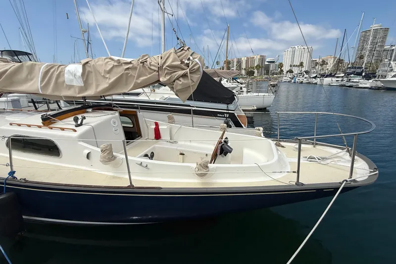1957 Rhodes Bounty sailboat docked in marina, surrounded by other boats and city skyline.