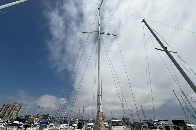 Sailboat masts against a cloudy sky, featuring a 1957 Rhodes Bounty model.