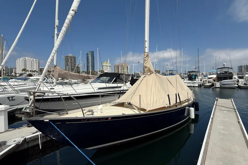 1957 Rhodes Bounty sailboat docked in marina with city skyline background.