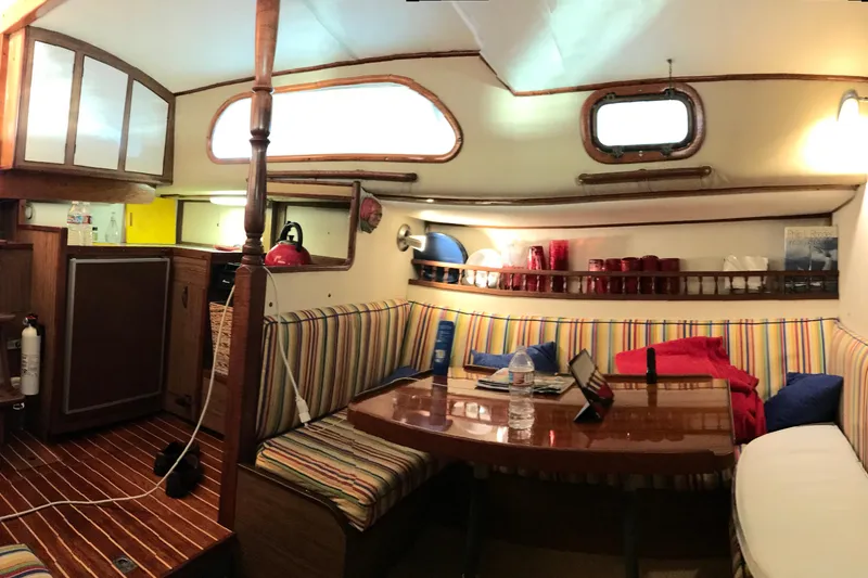 1957 Rhodes Bounty yacht interior with striped seating, wooden table, and compact kitchen area.