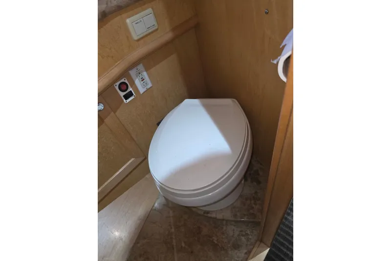 Toilet in 2000 McKinna 48 Pilothouse yacht bathroom, featuring wooden paneling and control switches.