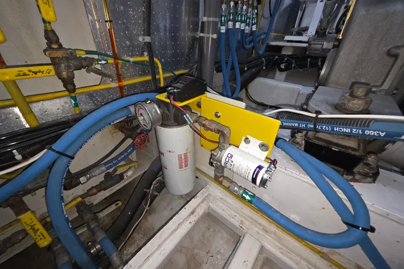 Engine room of 2000 McKinna 48 Pilothouse with hoses and mechanical components.