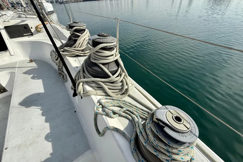 Deck of 1985 MacGregor 65 sailboat with winches and ropes by the water.