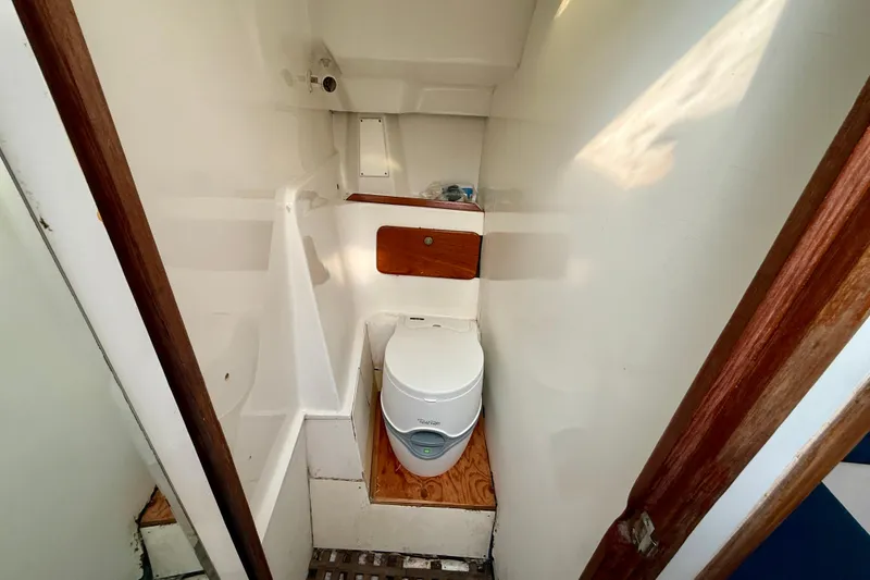 Compact bathroom in 1985 MacGregor 65 sailboat with portable toilet and wooden accents.
