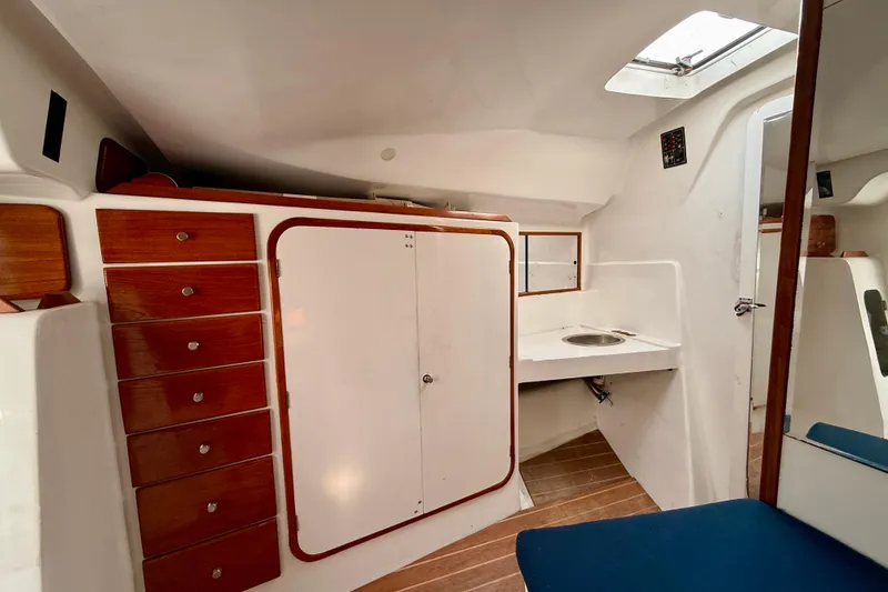 Interior of a 1985 MacGregor 65 sailboat with wooden cabinets and compact sink area.