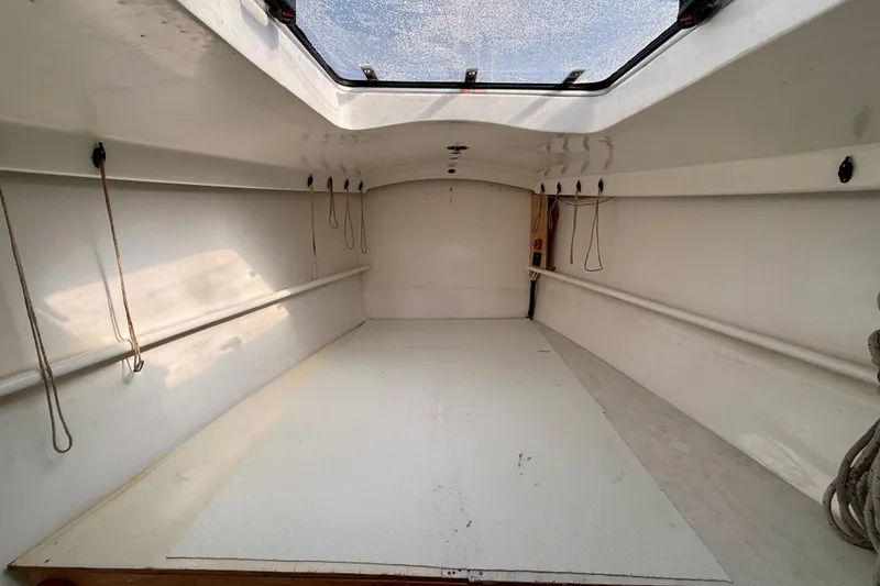 Interior of a 1985 MacGregor 65 sailboat, featuring a spacious, white cabin with ropes.