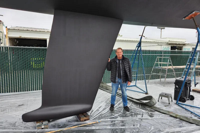 Man standing beside 1985 MacGregor 65 sailboat keel in a boatyard.