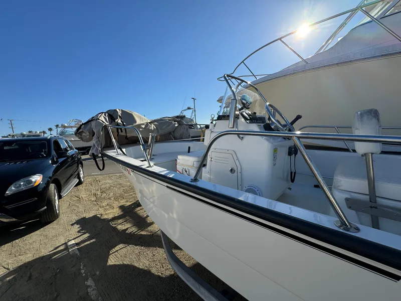 2016 Boston Whaler 170 MONTUCK boat parked beside a black car under clear blue sky.