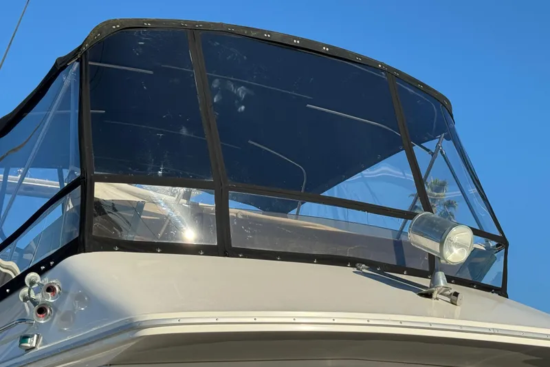 1990 Sea Ray 380 Aft Cabin boat with clear enclosure and spotlight, under blue sky.
