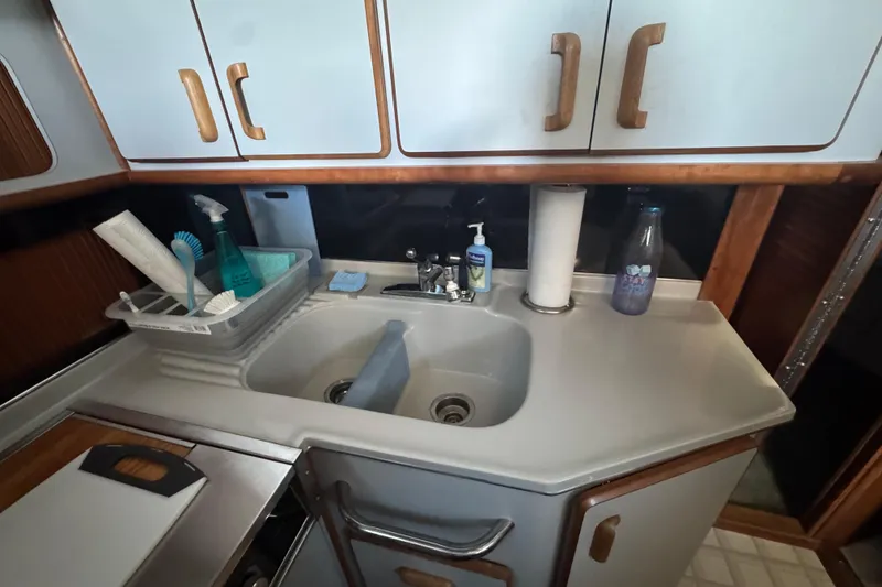 1990 Sea Ray 380 Aft Cabin kitchen sink with cleaning supplies and cabinets.