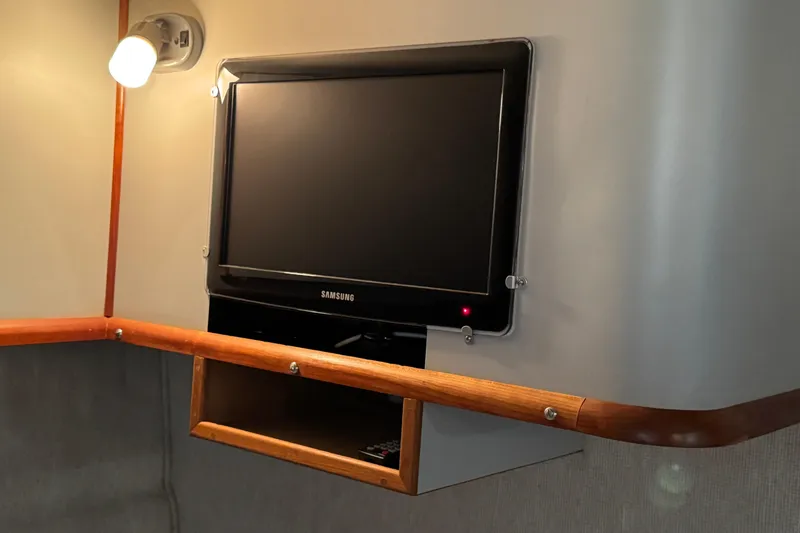 1990 Sea Ray 380 Aft Cabin interior with wall-mounted Samsung TV and wooden shelf.