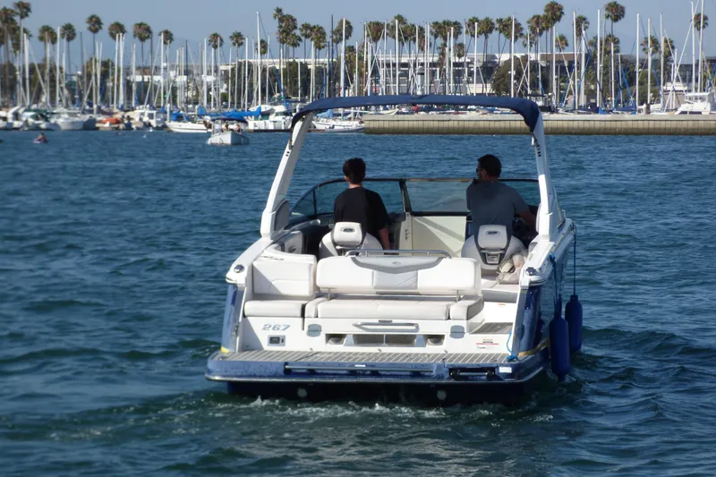 2018 Chaparral 267 SSX boat cruising in a marina with palm trees and sailboats.