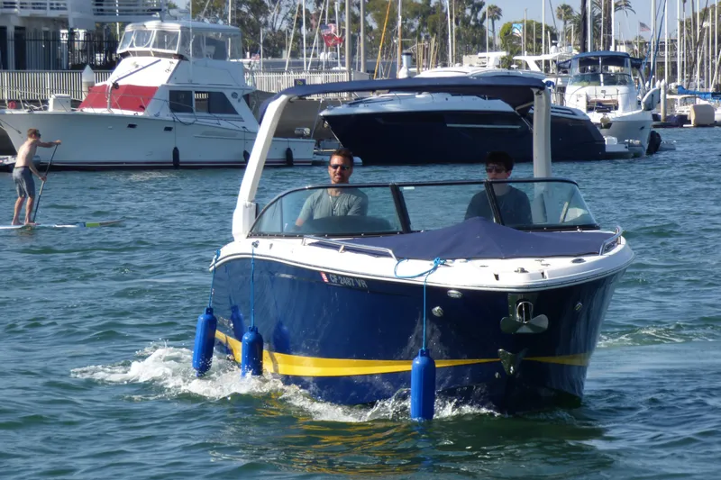 2018 Chaparral 267 SSX boat cruising in a marina with paddleboarder nearby.