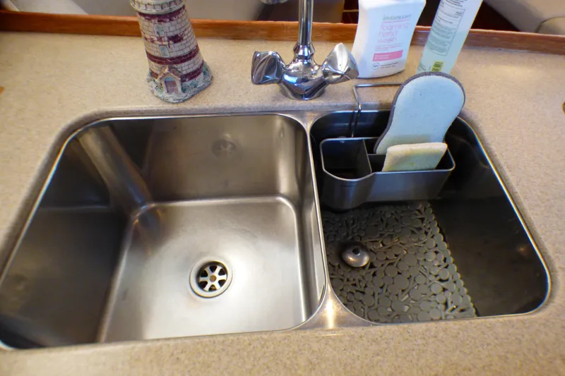 Stainless steel double sink with faucet and cleaning supplies on a 1993 Hunter 40.5 yacht.