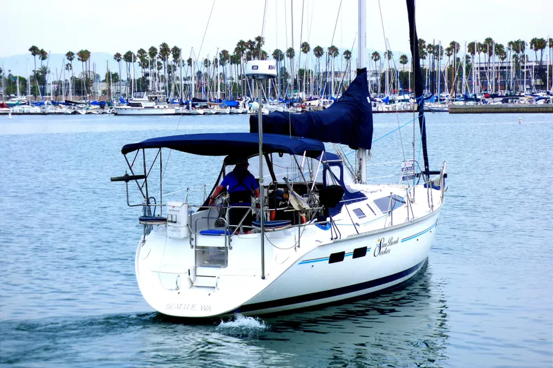 1993 Hunter 40.5 sailboat cruising in marina with palm trees and docked boats in background.