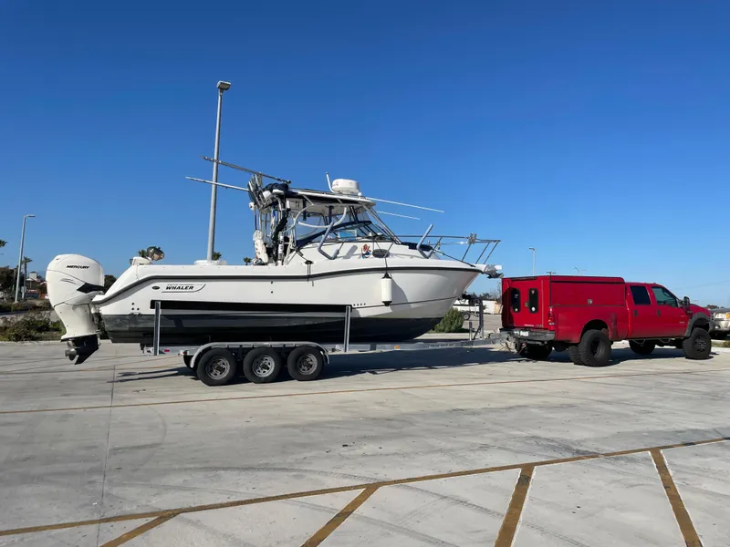 2008 Boston Whaler 285 Conquest boat on trailer, towed by red truck in parking lot.