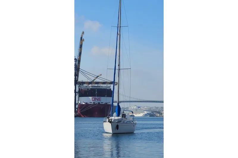 1987 O'Day 40 sailboat in harbor with cargo ship and cranes in background.