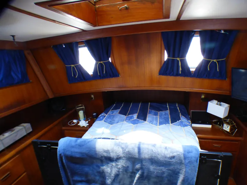 1980 CHB Heritage 42 Trawler cabin with bed, blue curtains, and wooden interior.