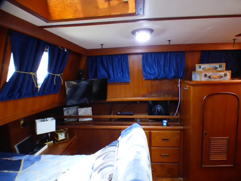 Interior cabin of 1980 CHB Heritage 42 Trawler with wooden furnishings and blue curtains.