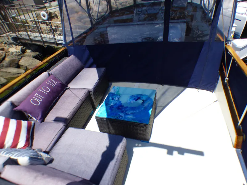 Outdoor seating area on a 1980 CHB Heritage 42 Trawler with a blue table and Out to Sea pillow.