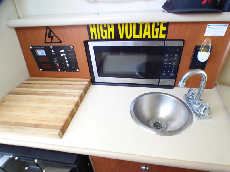 2004 Robalo R265 Walkaround kitchen with microwave, sink, and cutting board.