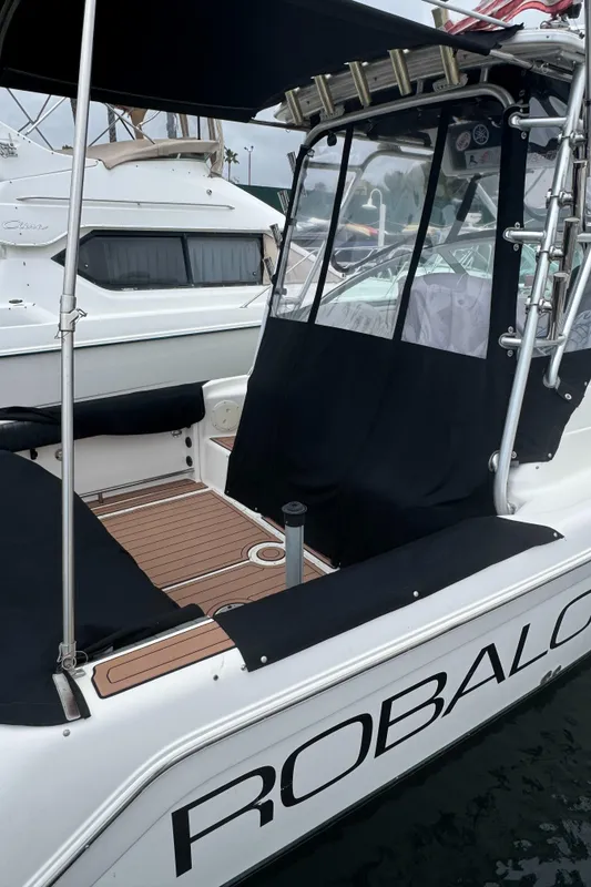 2004 Robalo R265 Walkaround boat with black canopy and seating, docked in a marina.