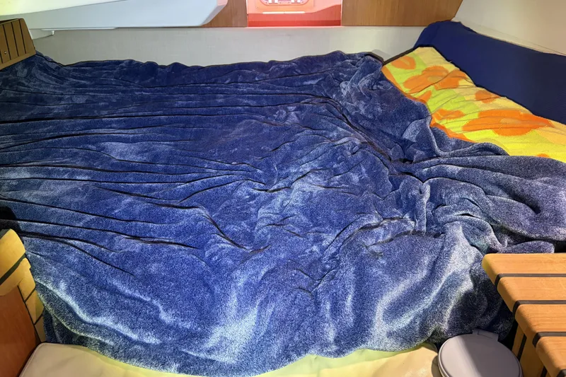 Cozy cabin bed with blue blanket in 2010 Beneteau Oceanis 37 sailboat.