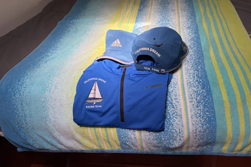 Blue "California Dream" racing team apparel on striped towel, featuring Adidas cap and Terrex jacket.